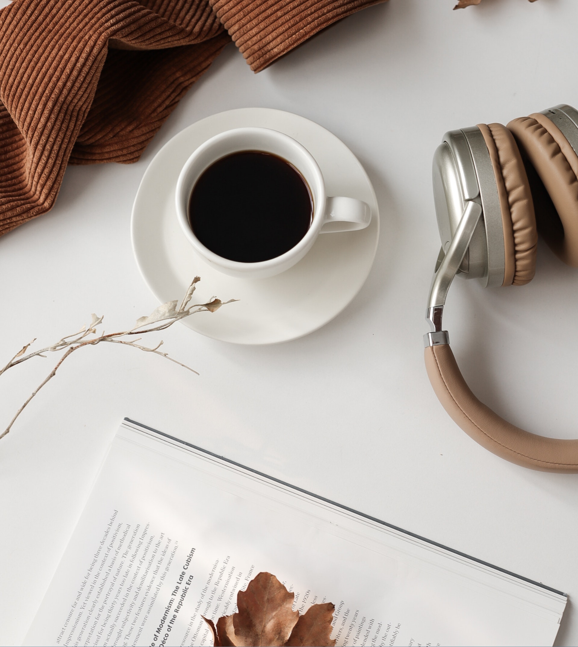 overhead photo of a cup full of black coffee with an opened book and headphones off to the side